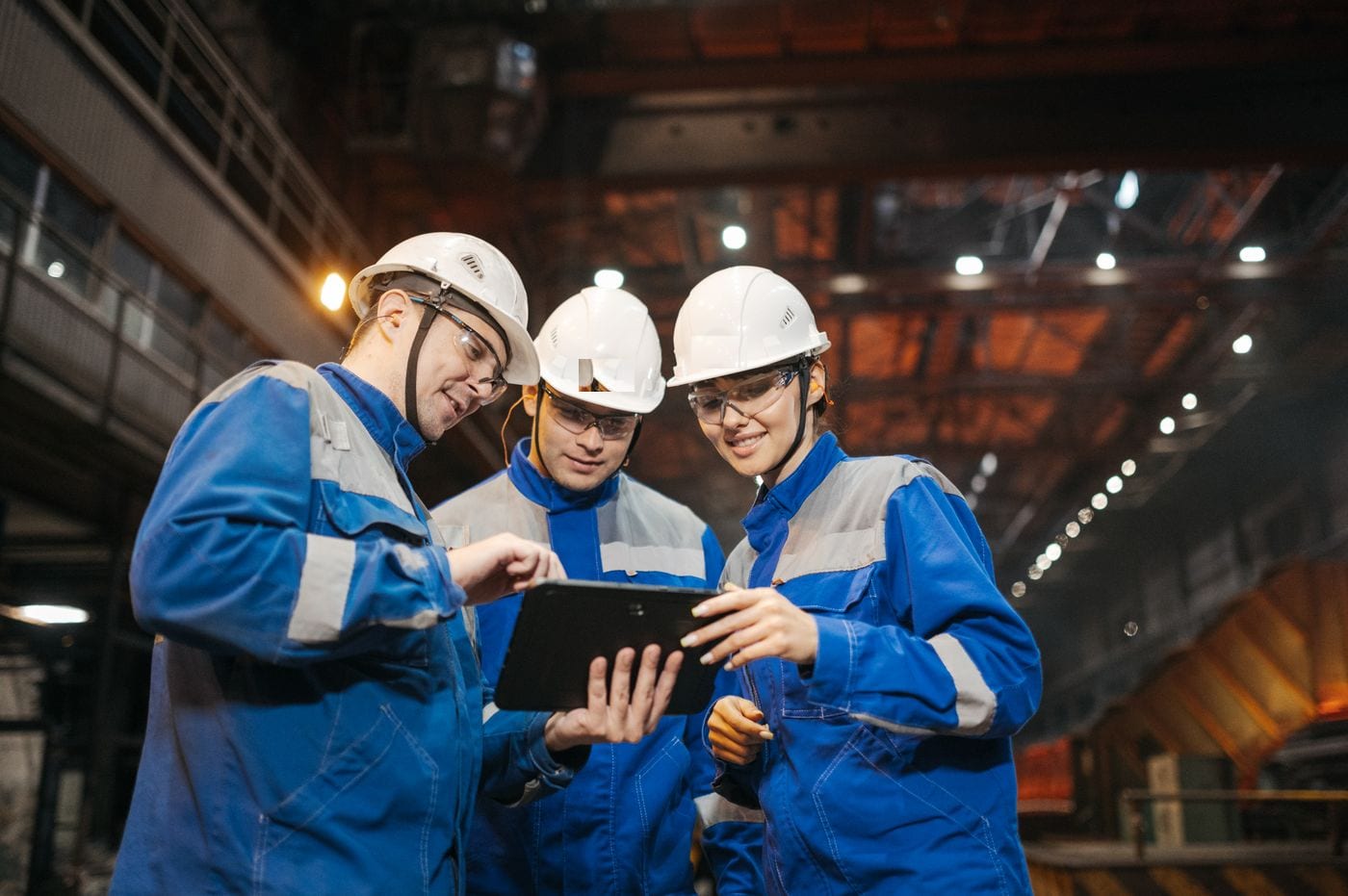 Operarios con casco revisando datos de producción en una tableta dentro de una planta industrial